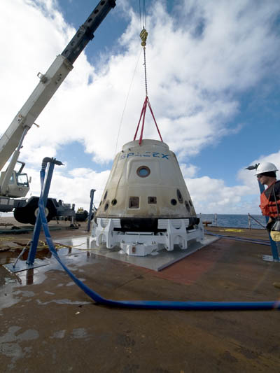 The SpaceX crew pictured bringing Dragon back to the barge where aDragon depicted in orbit, with its retractable solar panels. Image courtesy of SpaceX  crane lifted it from the water after Dragon went into orbit last year. Credit: SpaceX/Mike Altenhofen