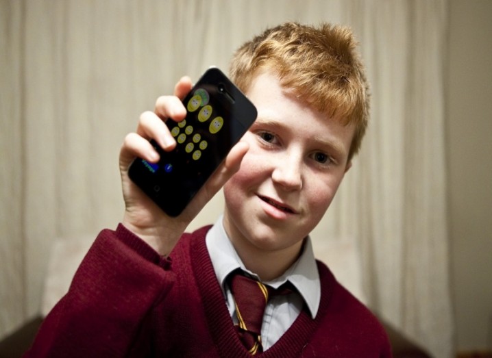 A young boy in a school uniform holds up an iPhone.