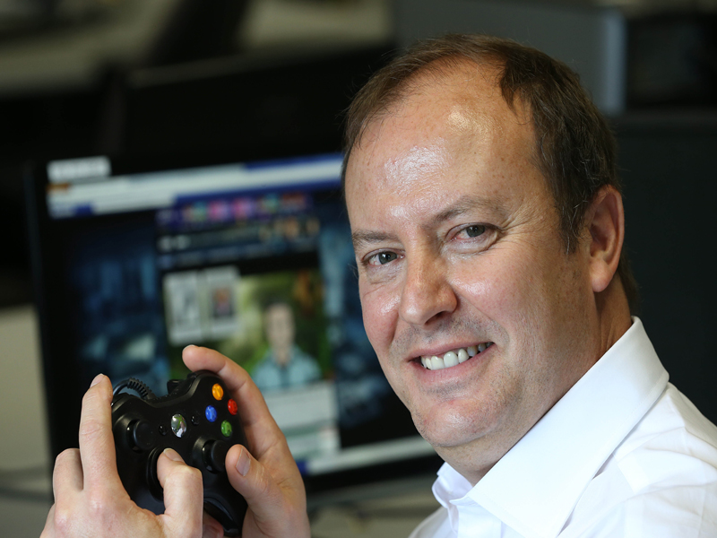 Andrew Day smiling holding a game console controller. 