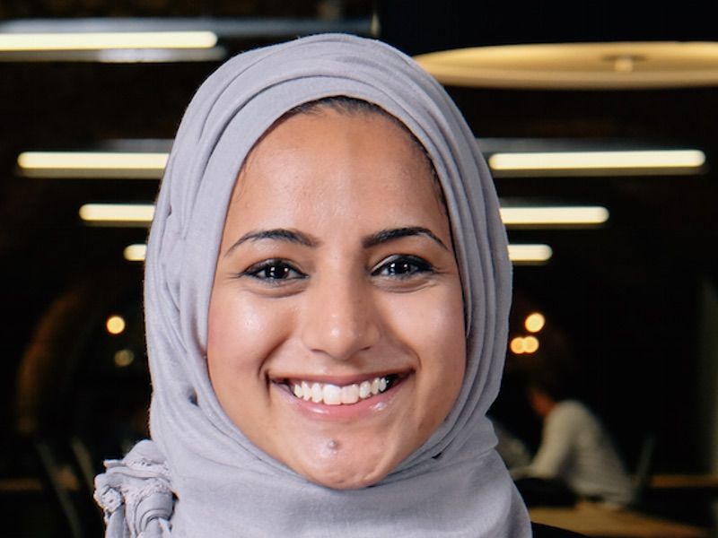 Headshot of a broadly smiling woman wearing a grey headscarf.