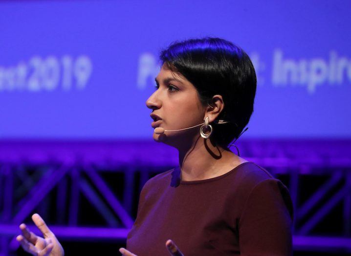 Woman with short black hair and maroon top speaking on stage in front of a purple background with the words Inspirefest 2019 on it.