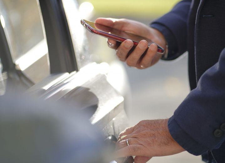 Closeup of a man in blue jacket unlocking door system of his car with a smartphone.