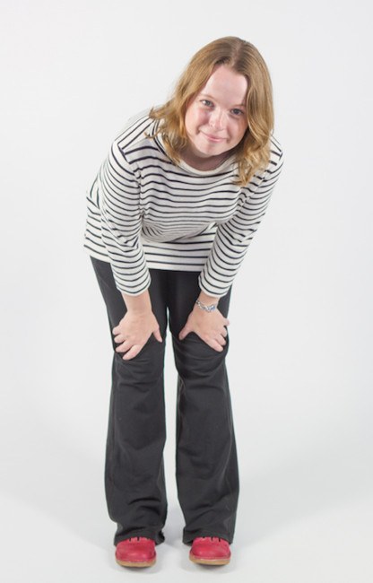 blonde woman wearing white and black stripy top bending down to look at the low-facing camera.