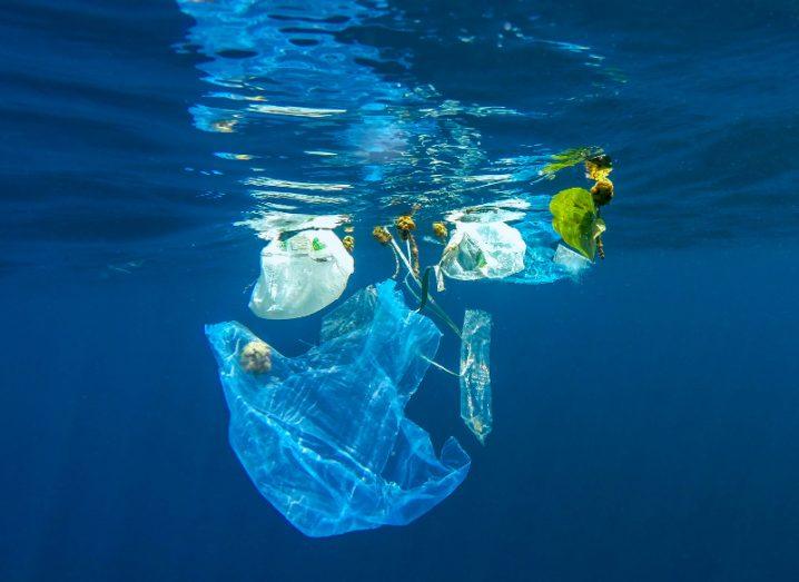 empty plastic bag and other debris floating near the surface of a bright blue ocean, symbolising the scourge of single-use plastics.