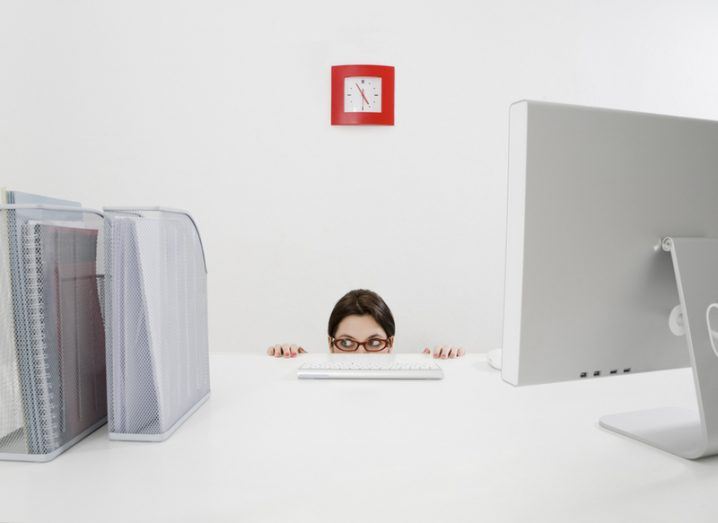 woman wearing glasses hiding behind desk in office
