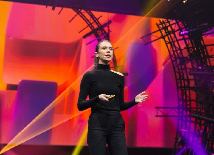 A woman in a black polo neck and trousers delivers her pitch on stage at Slush against a colourful backdrop.