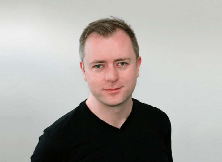 Man with short hair and dark t-shirt in front of grey background.