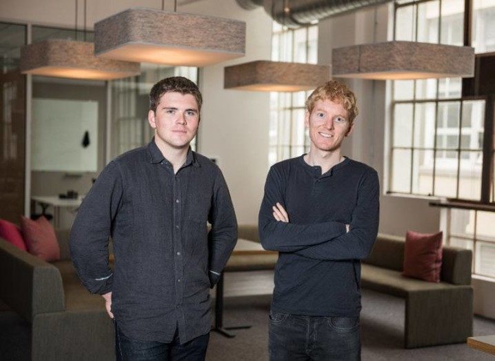 John and Patrick Collison stand side by side in an empty office foyer.
