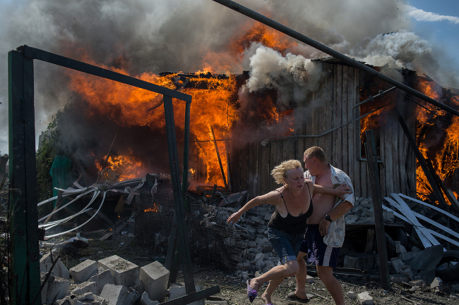 Civilians escape from a fire at a house destroyed by an air attack in Donbass, a village in Luhanskaya, eastern Ukraine – image via Valery Melnikov, photojournalism single image winner at Magnum and LensCulture Photography Awards 2016