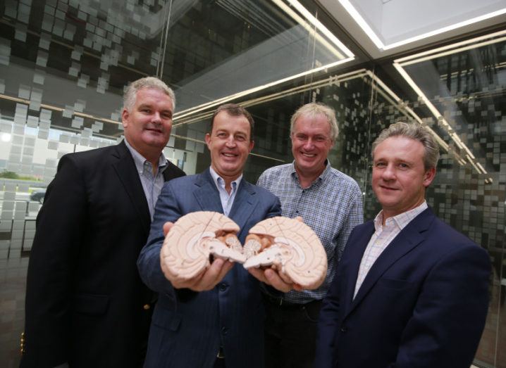 Four men from the Inflazome team stand in a glass room holding a model of a human brain.