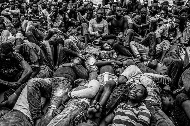 Gambian and other West African migrants lay exhausted on the deck of the Migrant Offshore Aid Station ship after being rescued from a packed rubber boat that was starting to sink off the coast of Libya. Image: Jason Florio. Photojournalism Series Winner, Magnum and LensCulture Photography Awards 2017.