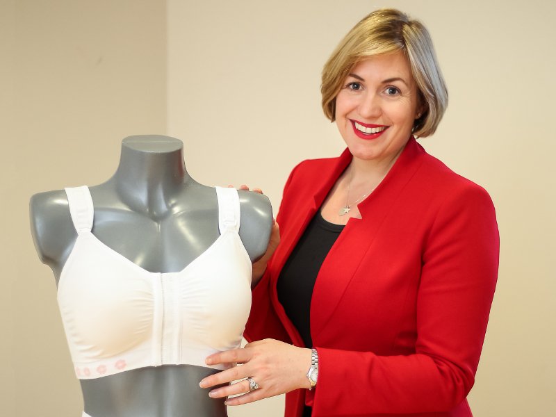 Ciara Donlon in red blazer standing next to one of her post-surgical bra products on a mannequin