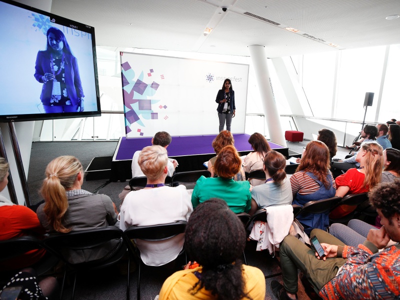 Researchfest finalist Bhagya Rekha Jonnala stands on a purple Inspirefest-branded stage presenting her research to a captive audience