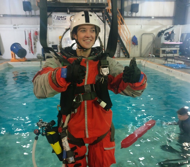 Norah Patten gives a thumbs up in a training spacesuit and harness as she is suspended knee-deep in a pool of water