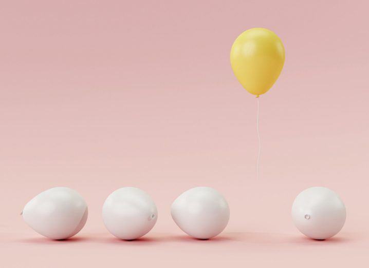 four white balloons on the ground with one yellow one floating - odd one out