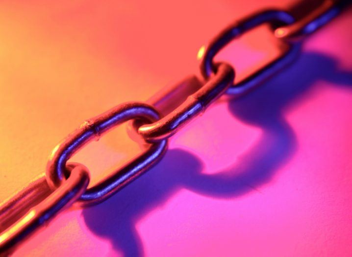 Close-up of links in a steel chain on a brightly coloured background of orange and pink hues