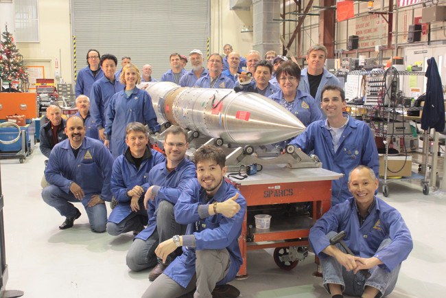 team in blue overalls gathered around rocket