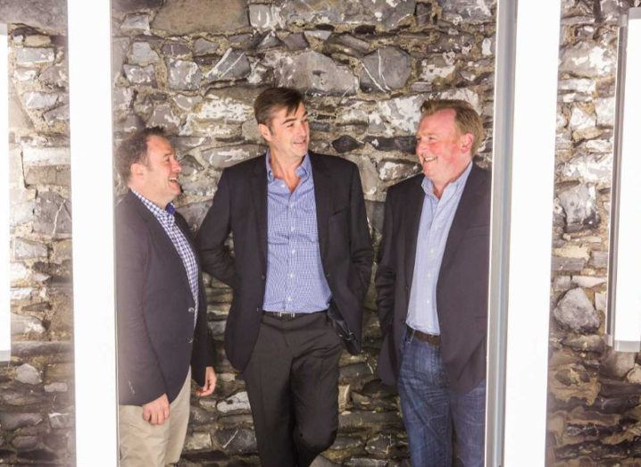 Urbanvolt founders Declan Barrett, Kevin Maughan and Graham Deane are standing against a brick wall surrounded by lights.