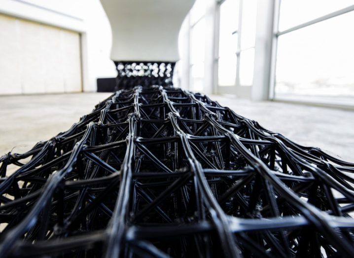 The black latticed base of a 3D-printed white bench with a large window in the background.