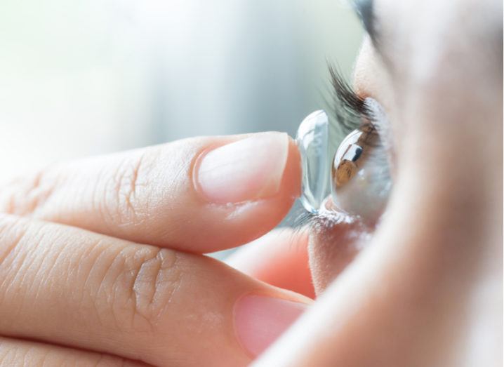 Close-up of a woman holding a contact lens on her finger as she places it in her eye.