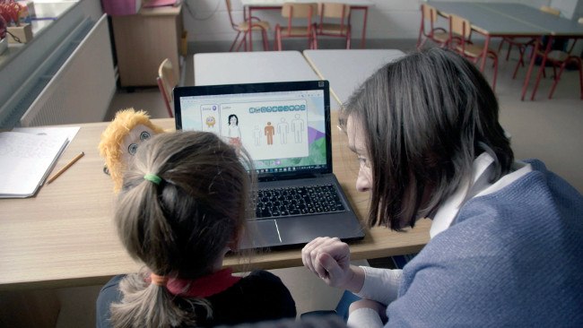 adult teaching a child Education Desty programme using laptop and yellow fuzzy toy.