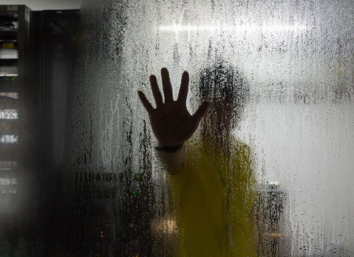 A mystery figure with hand on glass inside a data centre.