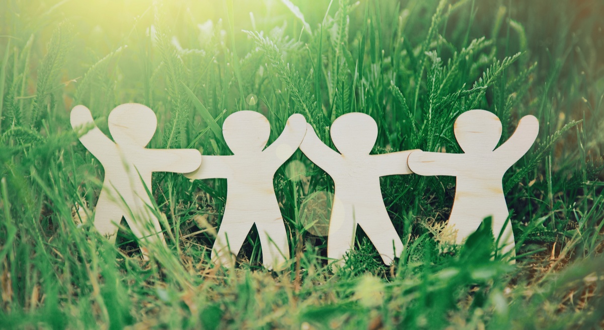 Wooden figurines standing in grass, holding hands symbolising HR companies working together to make the world better.