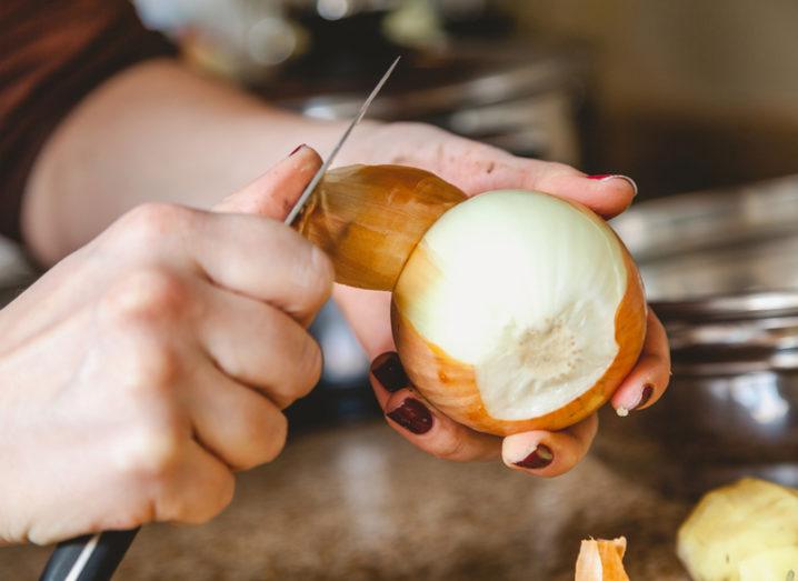 Close-up of a person's hands over a kitchen counter-top as they peel an onion with a knife.