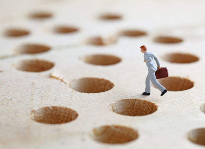 A miniature figure carrying a briefcase trying to navigate its way through a hole-covered floor.
