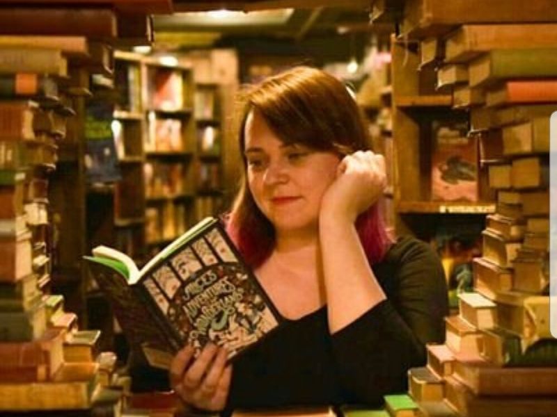 Sexuality studies researcher Caroline West is framed by a circle of books, reading Alice’s Adventures in Wonderland
