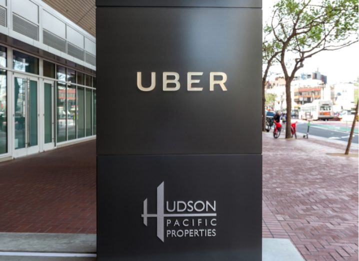 Uber logo on a black column outside its offices in San Francisco, trees in the background.