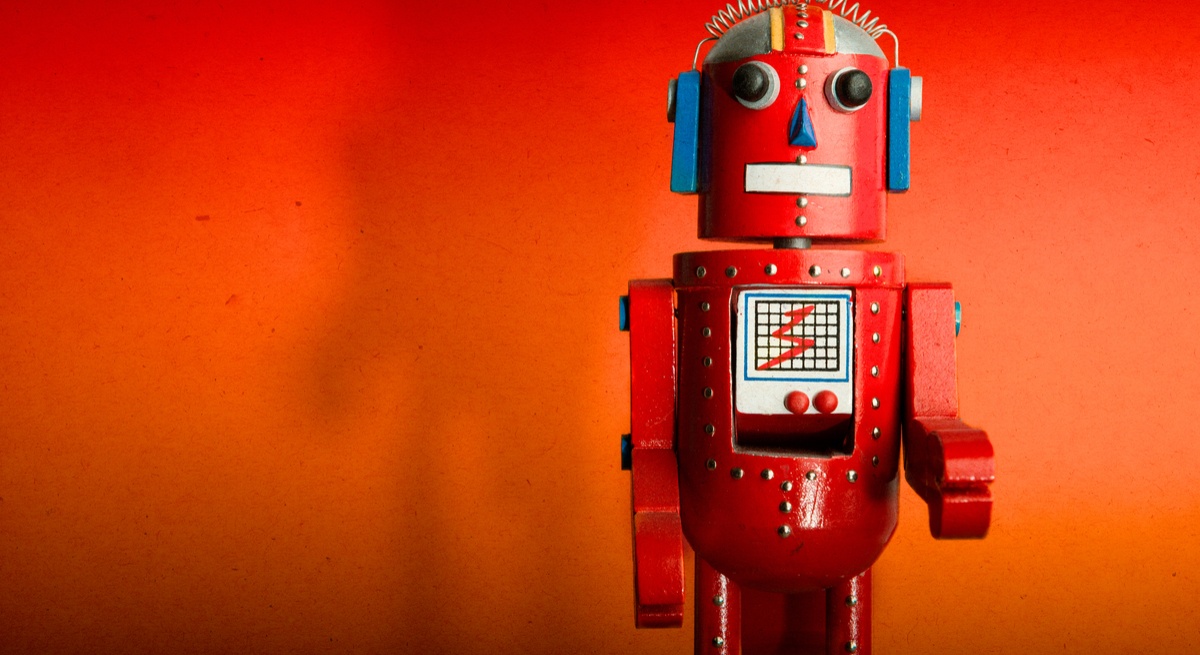 A red toy robot facing the camera. It is standing against an orange-red background.