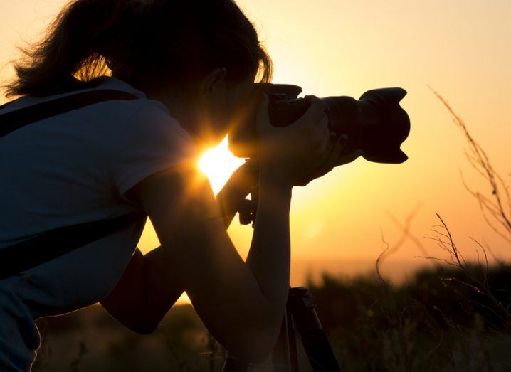 Silhouette of a woman taking a photograph at sunset with a long range lens.