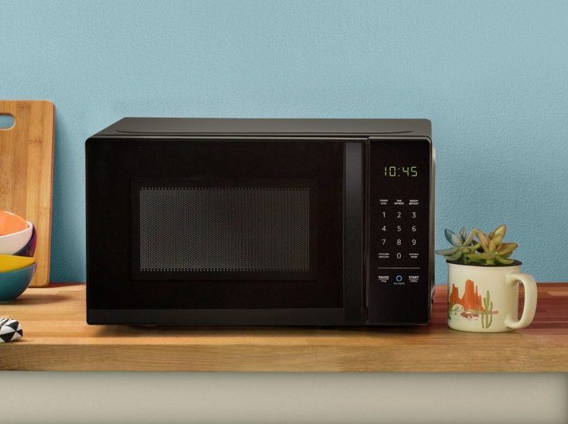 AmazonBasics microwave on a wooden counter in front of a blue wall.