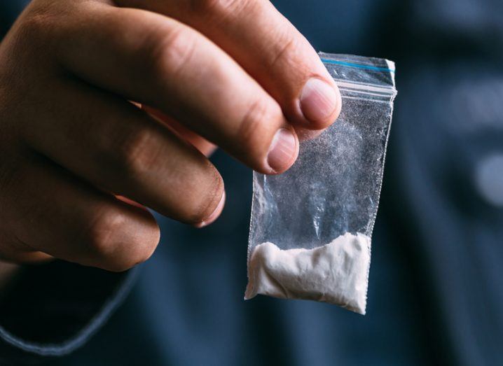 Close-up of hand holding a small, clear plastic bag filled with cocaine.
