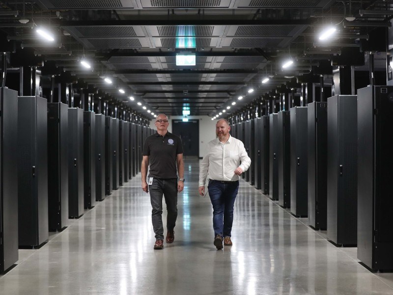 Two men walk between rows of servers in a data centre.