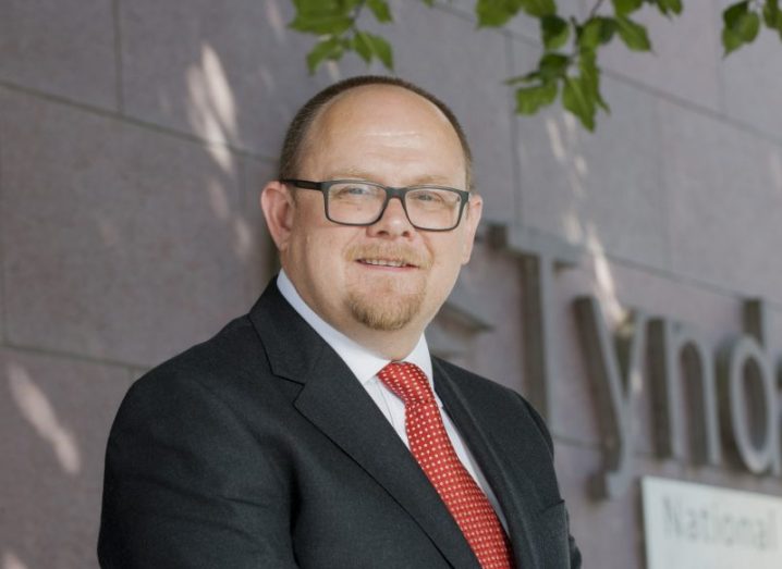 Prof William Scanlon wearing a black suit and red tie, outside the Tyndall National Institute building.