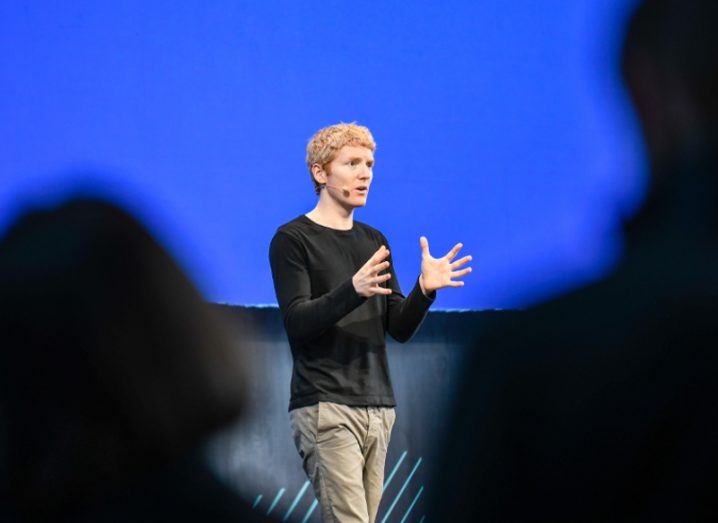 Man with black T-shirt and red hair addresses a crowd.