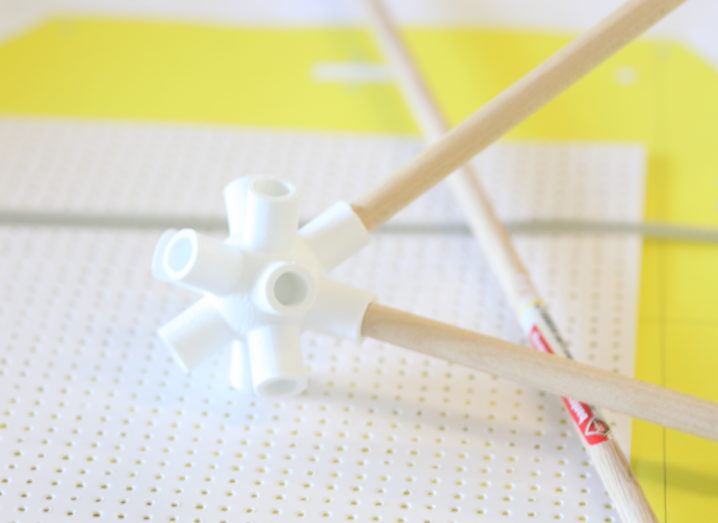 white plastic connector holding two wooden sticks balanced on white dotted paper on bright yellow surface.