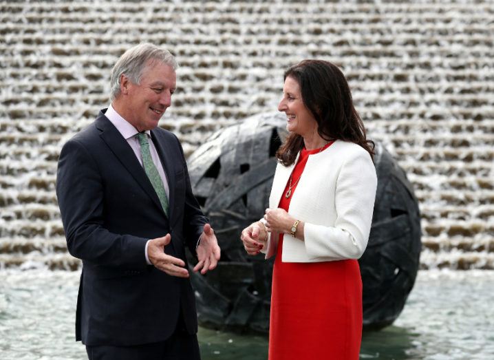 A well-dressed man and woman standing and talking in front of a fountain.