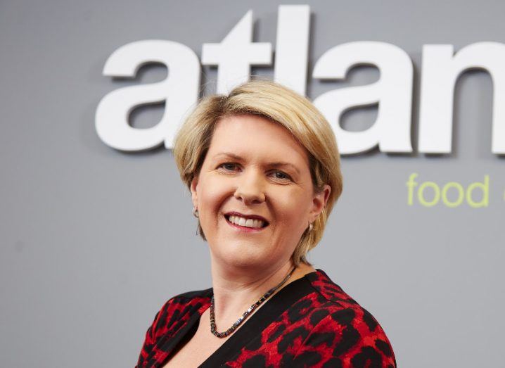 middle-aged woman with short blonde hair wearing red and black leopard print top and smiling, against grey wall with atlantia logo in white.