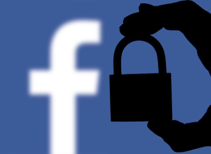 A hand holds a padlock in front of the Facebook logo.