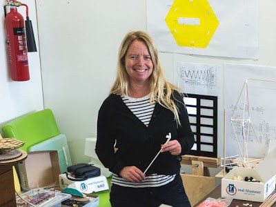 woman with long blonde hair wearing white and black striped tshirt and black cardigan standing in a studio and smiling.