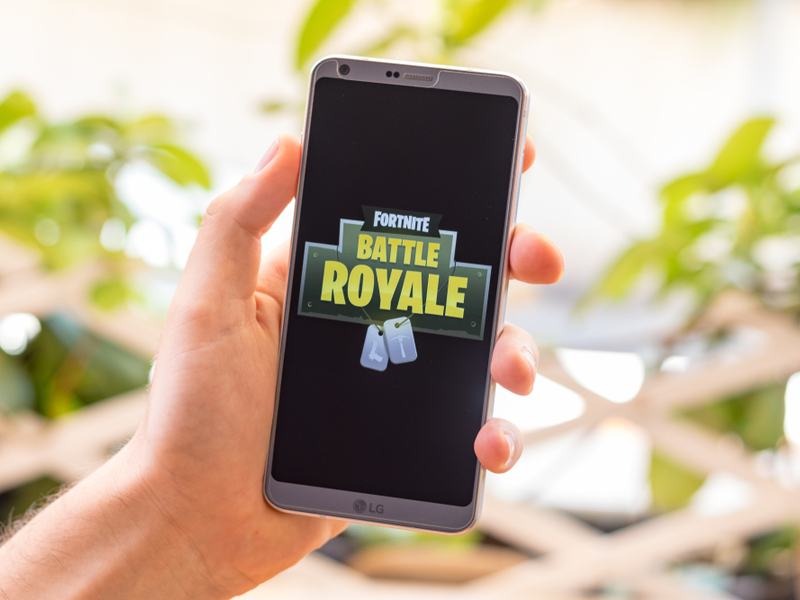A mobile phone showing the Fortnite Battle Royale game logo with bright lights in the background.