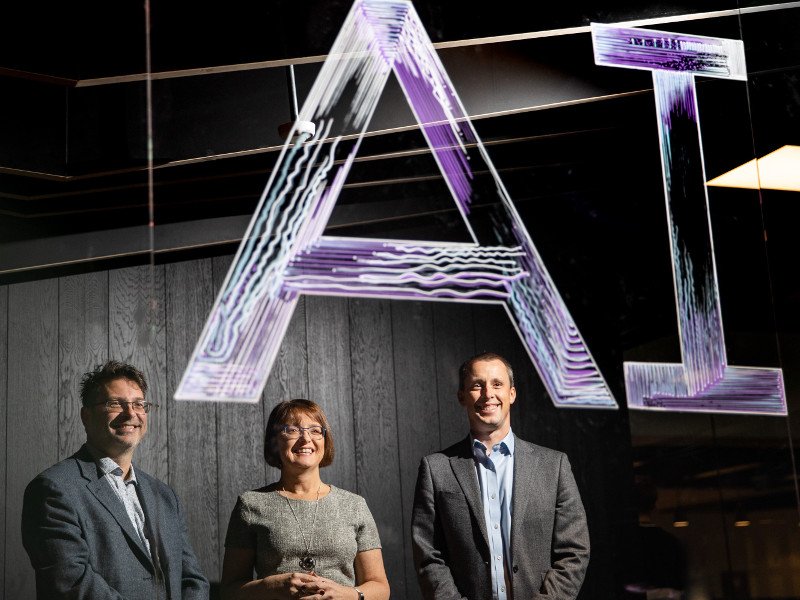 Two men and a woman stand under a purple neon sign emblazoned with the words AI.