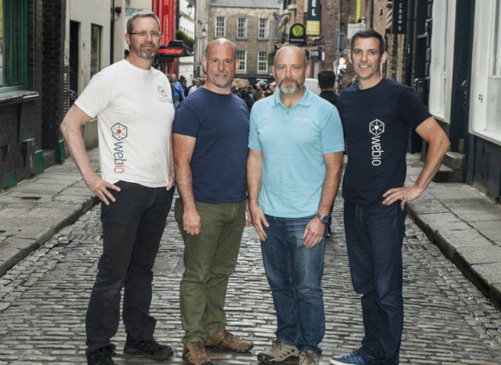 Four men in T-shirts stand on a cobbled street in Dublin.