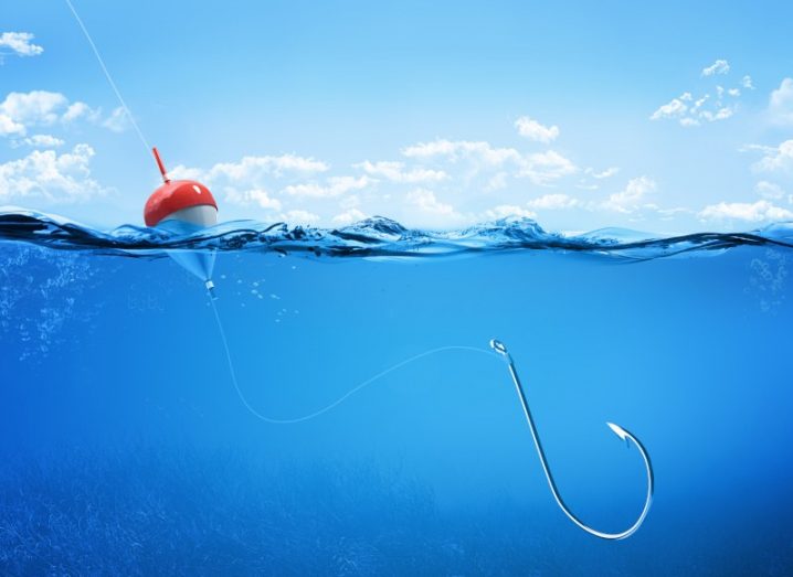 A steel fishing hook underwater with red bait on the surface.