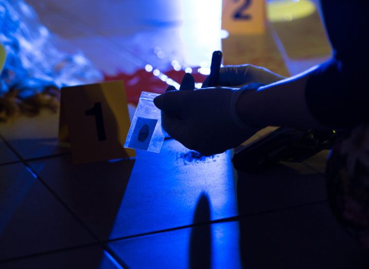 The gloved hands of a forensic investigator collecting evidence from a crime scene, the intersection of protecting society and genetic privacy.