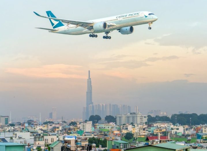 A Cathay Pacific plane flying over Ho Chi Minh City, Vietnam with skyscrapers in the background.