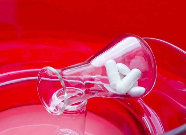 Glass beaker with pharma pills emptying into a petri dish against a vibrant red background.